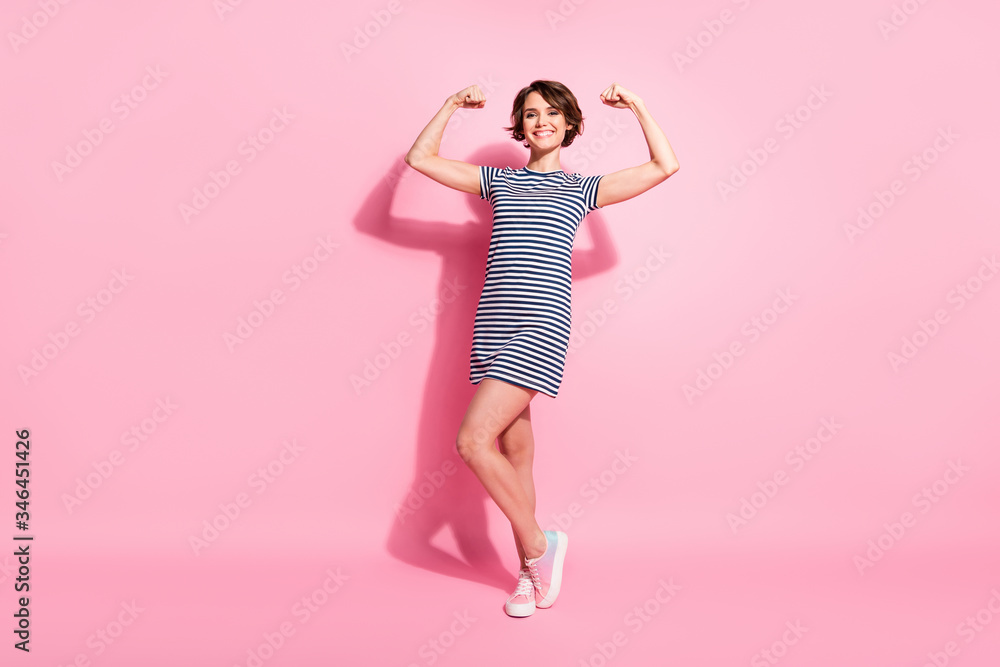 Full body photo of pretty lady skinny shapes good mood showing perfect biceps after gym workout wear casual white blue striped mini summer dress isolated pastel pink color background Full body photo of pretty lady skinny shapes good mood showing perfect biceps after gym workout wear casual white blue striped mini summer dress isolated pastel pink color background