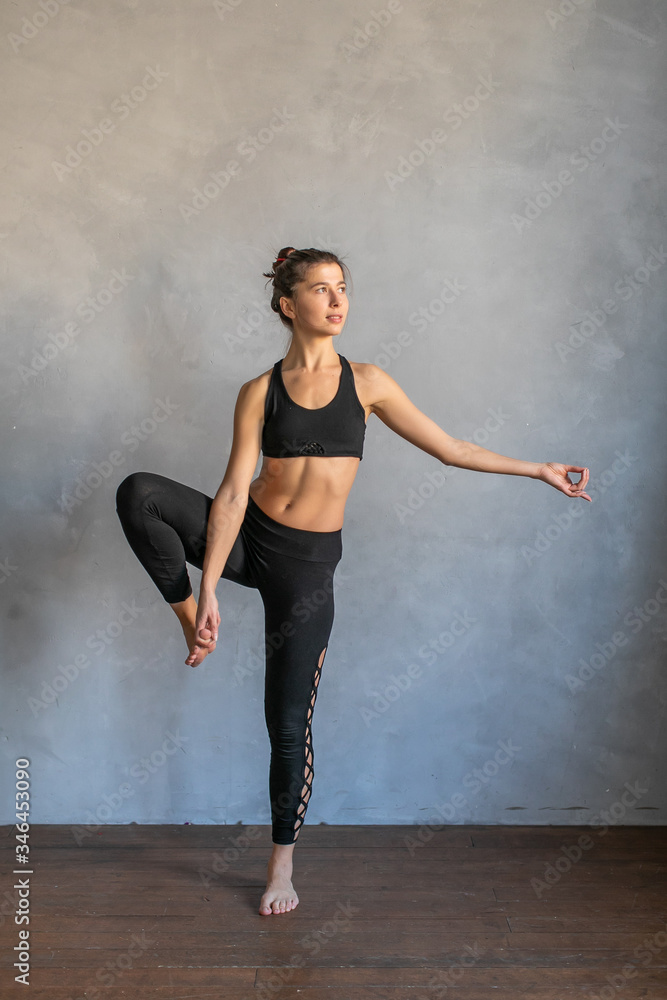 Young woman standing in a yoga exercise position. Girl balancing, practice stretch exercise at yoga class - she is standing on one leg Young woman standing in a yoga exercise position. Girl balancing, practice stretch exercise at yoga class - she is standing on one leg