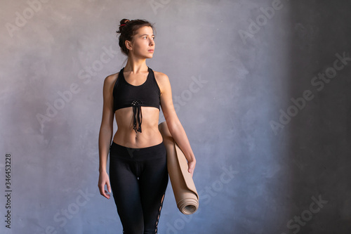 Woman standing at work out or yoga class with fitness mat in her hads. Copy space on dark background