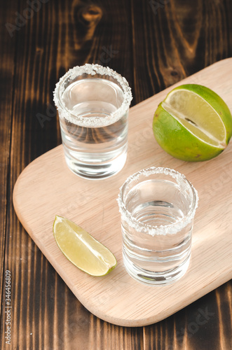 two Tequila shots with lime slices and salt on wooden table/Tequila shots and lime slice on wooden table. Top view