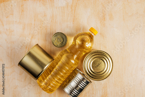 a bottle of sunflower oil and metal cans of various canned food on a light wooden background