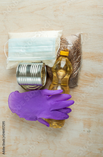medical protective equipment and long-term storage products on a light wooden background. medical mask, medical gloves and string bag on a bottle of sunflower oil and canned food