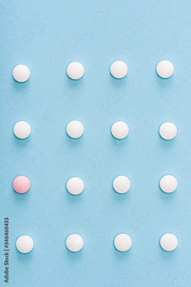 Flat lay with pink pill among white on blue background