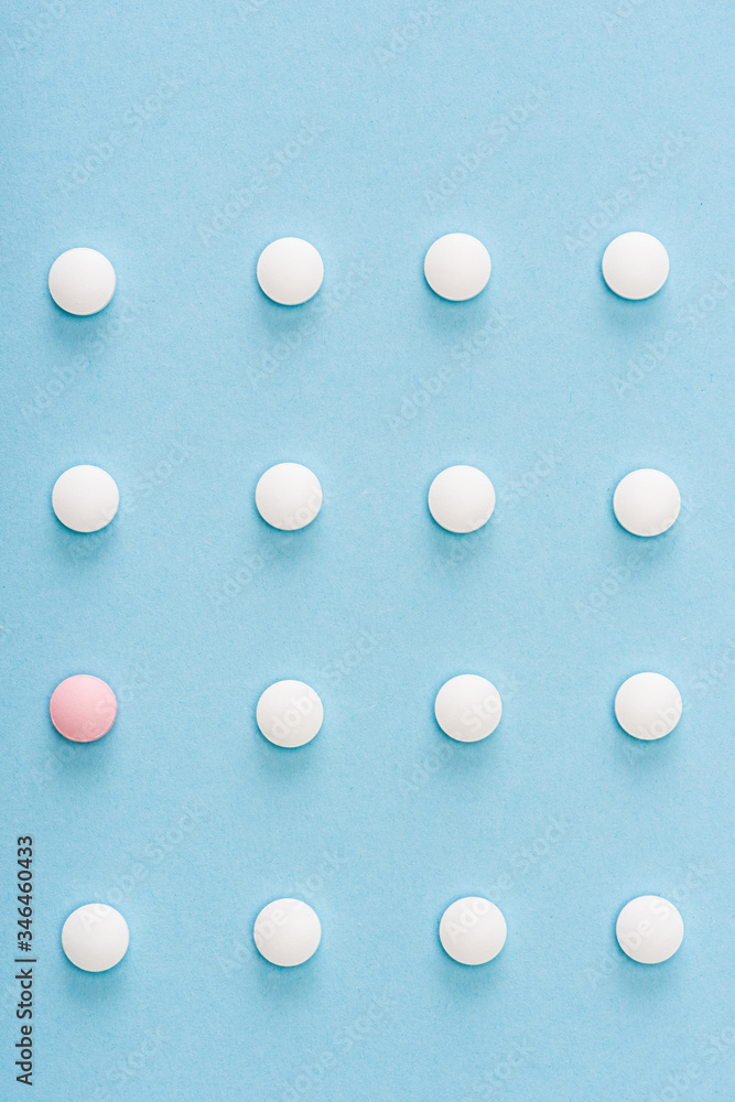 Flat lay with pink pill among white on blue background Flat lay with pink pill among white on blue background