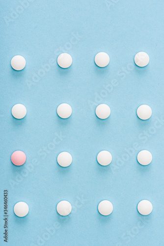 Flat lay with pink pill among white on blue background