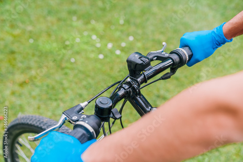 Person cycling outdoors in nature wearing blue latex gloves as a coronavirus prevention measure. Person holding the handlebars of the bicycle.