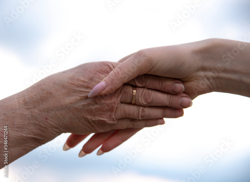 The hands of an elderly and young woman are joined together.