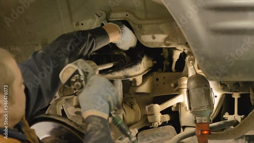 Hands in gloves and work clothes are repairing a spare part of a car in a garage, closeup.