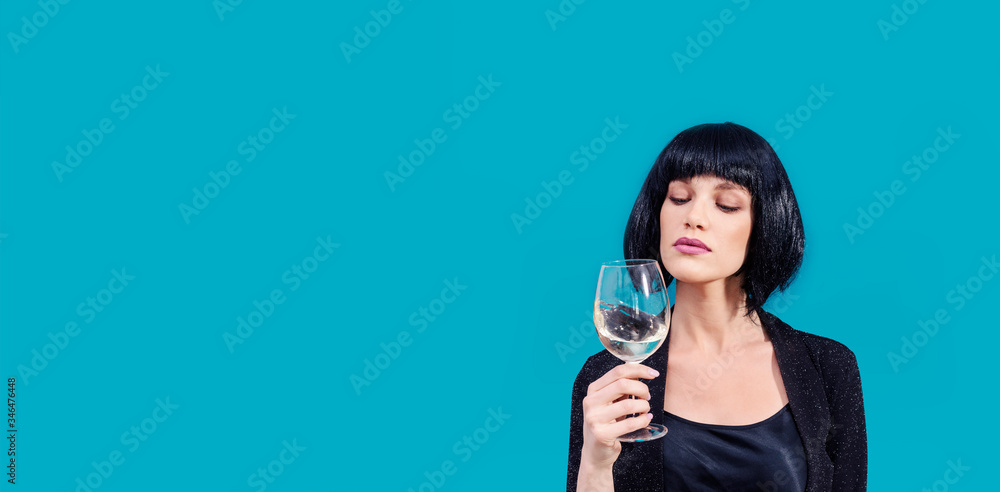 Fashionable woman is drinking and presenting glass of wine on a blue background Fashionable woman is drinking and presenting glass of wine on a blue background
