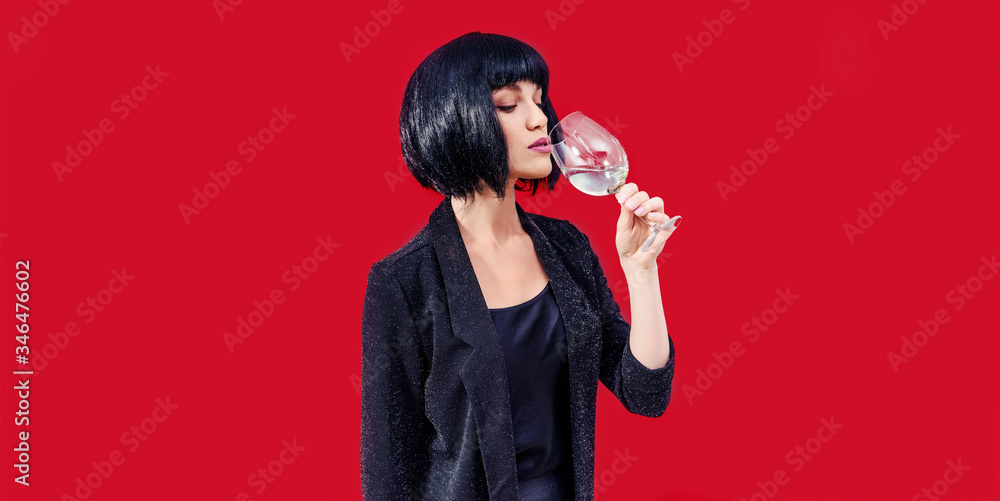 Fashionable woman is drinking and presenting glass of wine on a blue background Fashionable woman is drinking and presenting glass of wine on a blue background