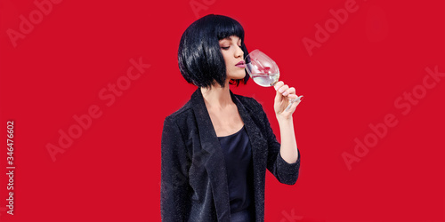 Fashionable woman is drinking and presenting glass of wine on a blue background