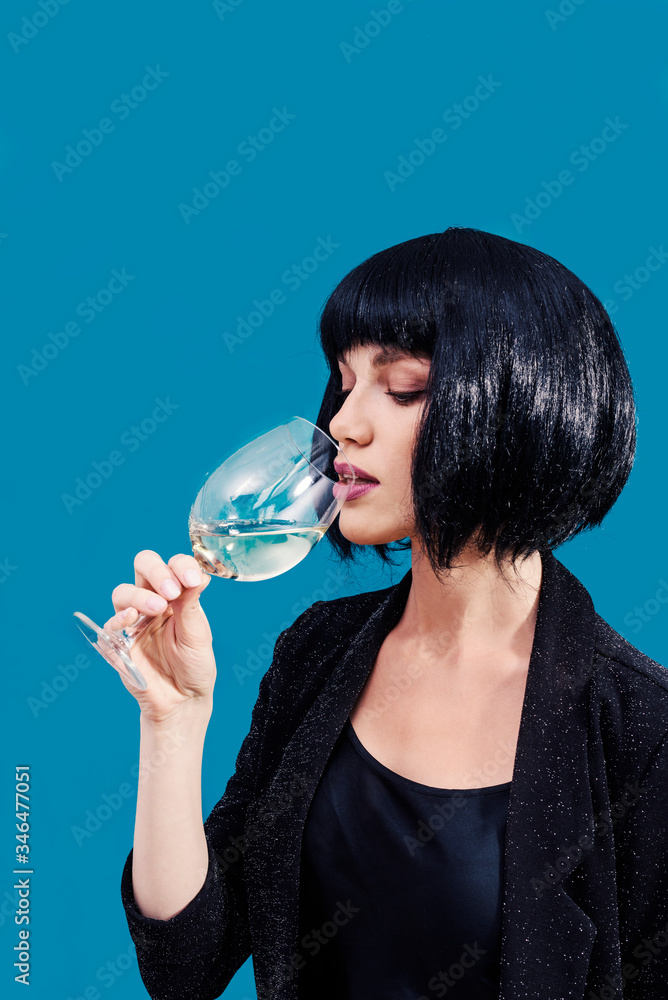 Fashionable woman is drinking and presenting glass of wine on a blue background Fashionable woman is drinking and presenting glass of wine on a blue background