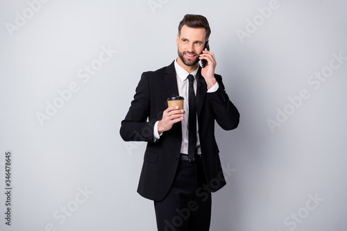 Portrait of positive agent man have work relax time hold take-out coffee beverage mug speak on cell phone colleagues family friends wear black pants blazer jacket isolated grey color background © deagreez