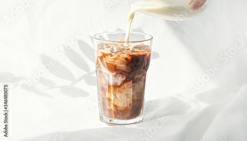 Milk cream is poured into a iced coffee cold brew.  Coffee cold drink with ice and milk.
