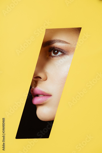 Female face with makeup in quadrangular hole in yellow paper on black © LIGHTFIELD STUDIOS