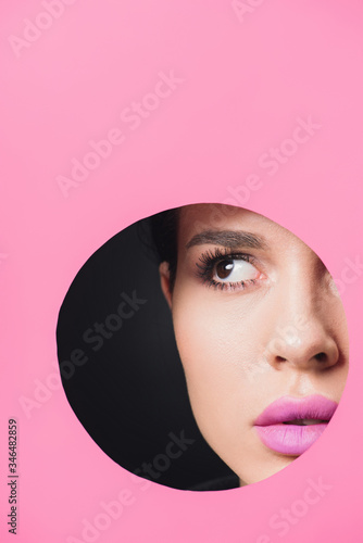 Beautiful girl with smoky eyes and pink lips looking away across round hole in paper on black background © LIGHTFIELD STUDIOS