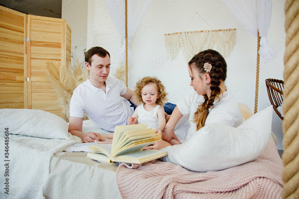 a child with his parents plays in bed at home. Mom and dad daughter posing in bed. Morning with your family.