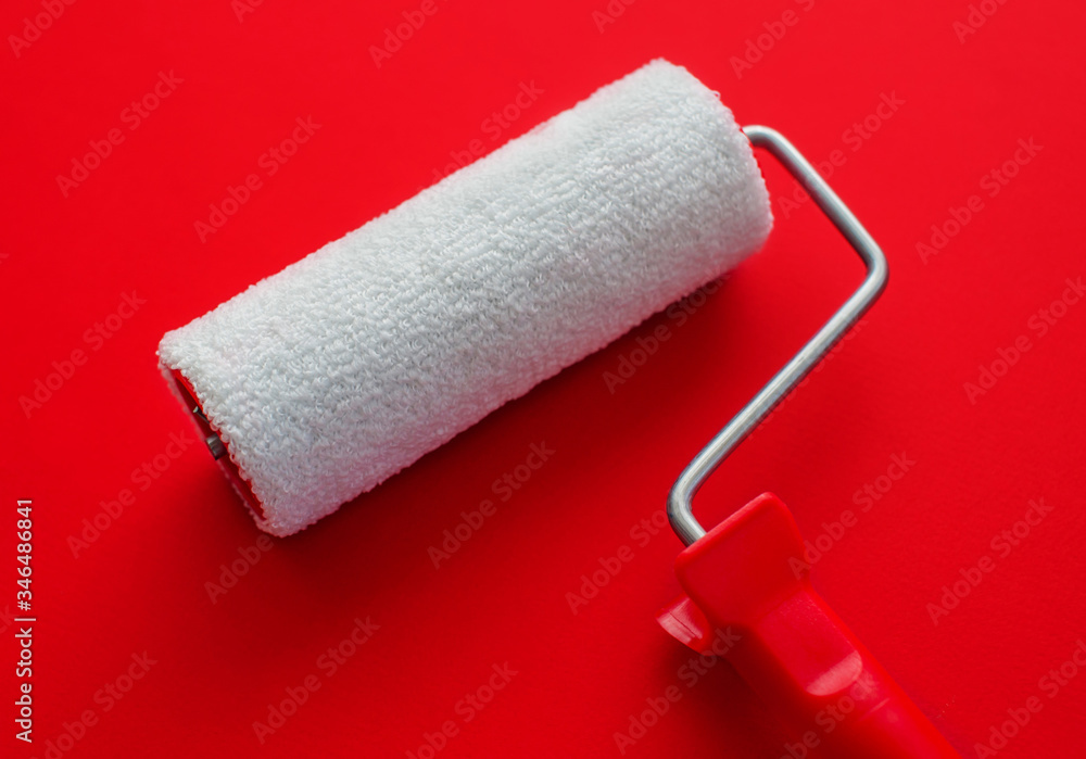 Obraz premium The concept of construction painting work. New clean white paint roller against red background