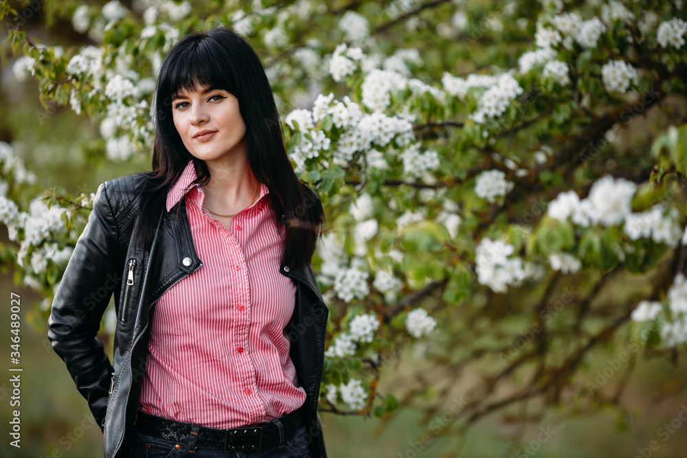 Beautiful young brunette girl near a flowering tree in a black leather jacket. Close-up. Copy space Beautiful young brunette girl near a flowering tree in a black leather jacket. Close-up. Copy space