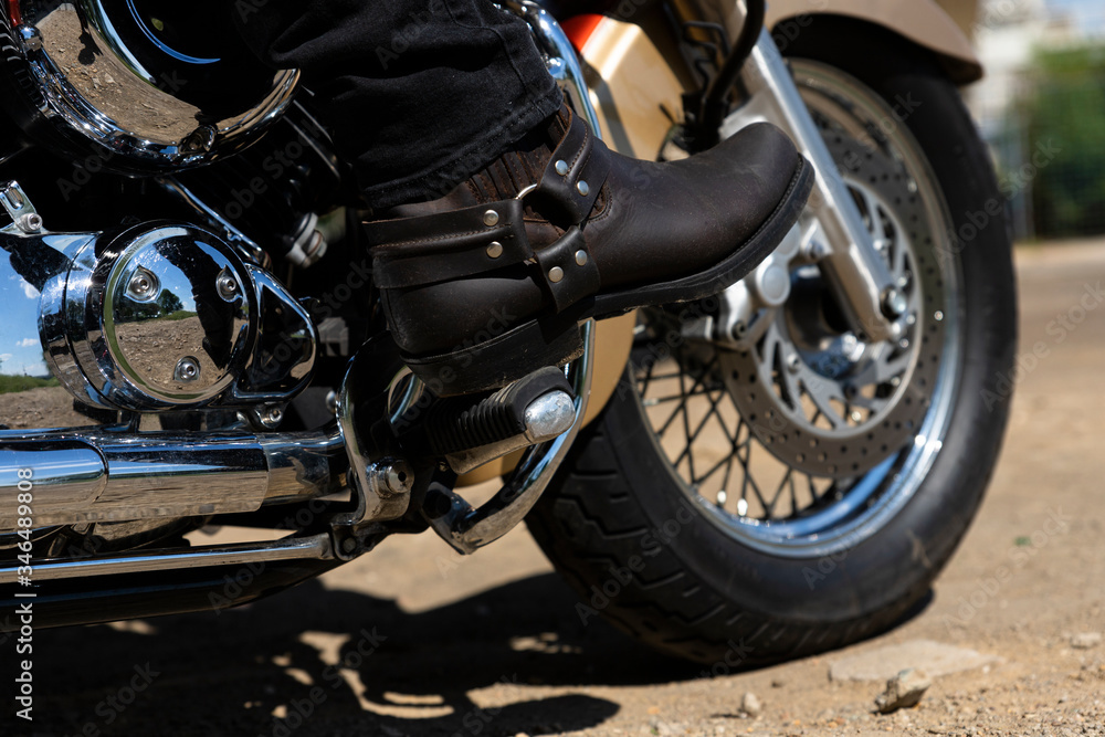 Biker riding a motorcycle. Bottom view of the legs in leather cowboy boots Biker riding a motorcycle. Bottom view of the legs in leather cowboy boots