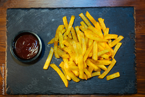 French fries cooked in a deep fryer with sauce on a black stone tray