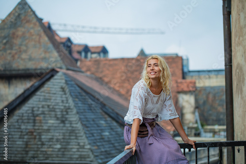 Woman an adult young beautiful and happy blonde on a balcony against the background of ancient roofs of a beautiful European city © kuzmichstudio