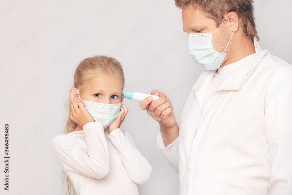 Man doctor in a medical mask measures the temperature of a girl child using an electronic thermometer on an isolated background