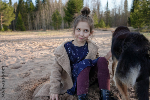  little girl plays with her dog on a sandy beach near the lake