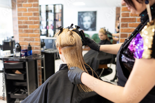 Hairdresser makes professional hair care to a young girl, blonde in a beauty salon. The interior of the beauty salon. Beautiful woman enjoys the care. View from the back