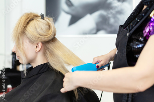 Beautiful blonde girl with long straight hair sits in a chair in a beauty salon. A professional hairdresser makes a girl curling after leaving and dyeing her hair. Blond hair with a comb close-up.
