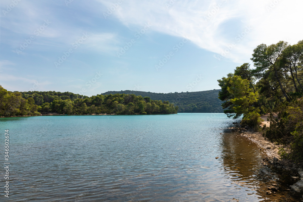 View of the saltwater blue colored lakes of malo and veliko jezero at the National Park on the island Mljet, Croatia. Mediterranean adriatic coast with a blue sky and greenery View of the saltwater blue colored lakes of malo and veliko jezero at the National Park on the island Mljet, Croatia. Mediterranean adriatic coast with a blue sky and greenery