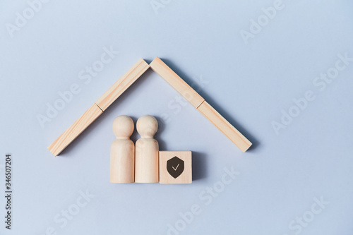 Family life and property insurance. Wooden figures family under house roof. Home building. Copy space. Isolated on blue