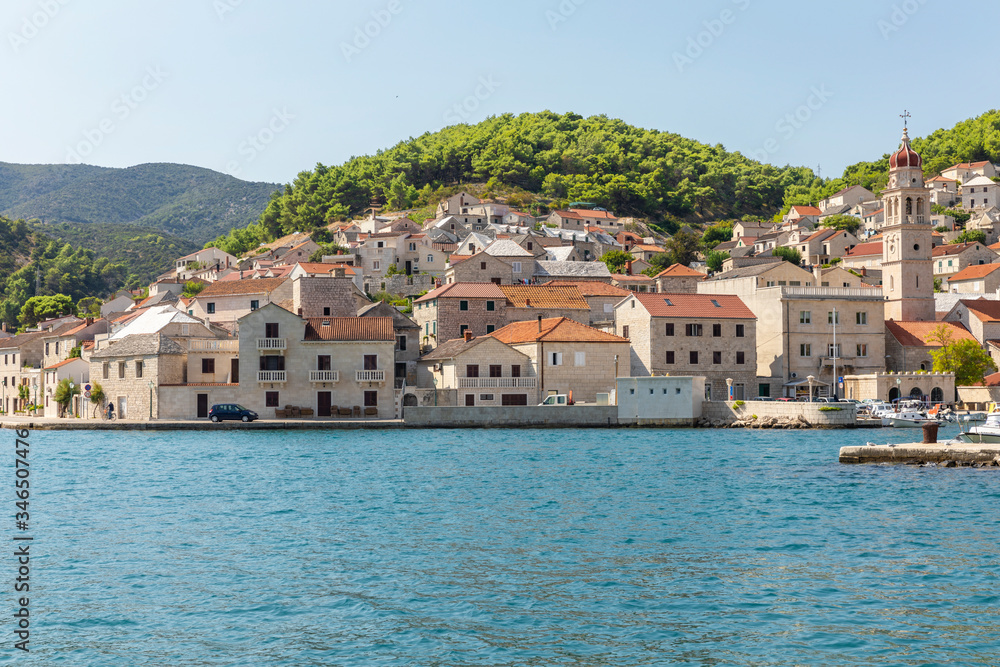 Pucisca town at Brac in Croatia, view from the sea on a sunny day in the summer. The port with it’s famous limestone from the island. Small idyllic place, village in Dalmatia. Holiday destination