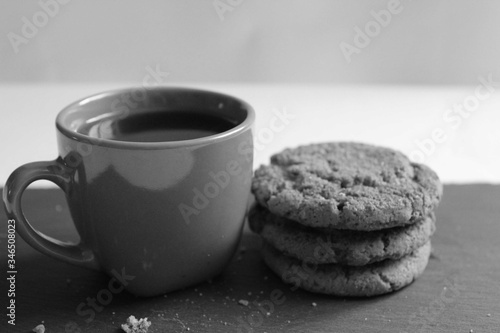 black and white still life a Cup of tea or coffee with a stack of homemade oatmeal cookies and sugar cubes on a white background