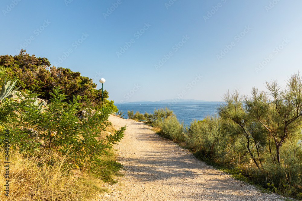 Makarska in Dalmatia, Croatia. View from the peninsula on a sunny day in summer with a blue sky. Rough nature, a path with greenery and rocks and the Adriatic sea at the Mediterranean coast