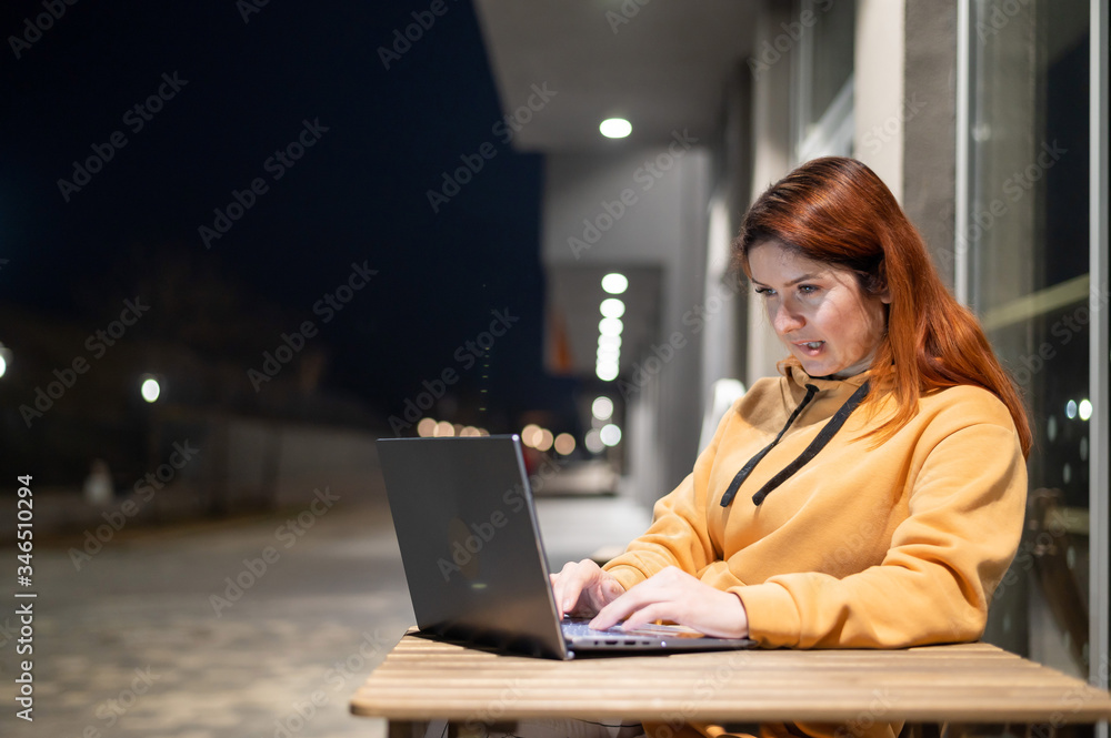A woman works remotely at a laptop in a summer cafe late in the evening. A smiling girl is studying while sitting down in a wasted street at a wooden table. A woman works remotely at a laptop in a summer cafe late in the evening. A smiling girl is studying while sitting down in a wasted street at a wooden table.