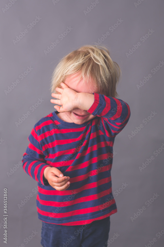 Little toddler child, boy, crying, hiding his face with hand, isolated image on gray Little toddler child, boy, crying, hiding his face with hand, isolated image on gray