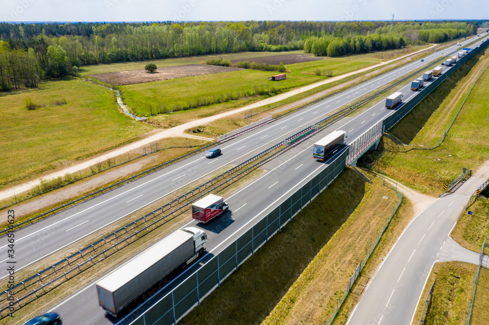 Aerial Follow Shot of White Semi Truck with Cargo Trailer Attached Moving Through Industrial Warehouse, Rural Area. Sun Shines and the Sky Are Blue.