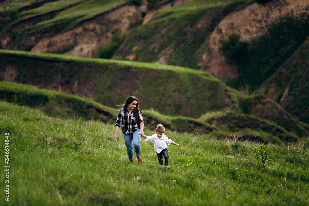 mom and baby run and cuddle in a green meadow, hills