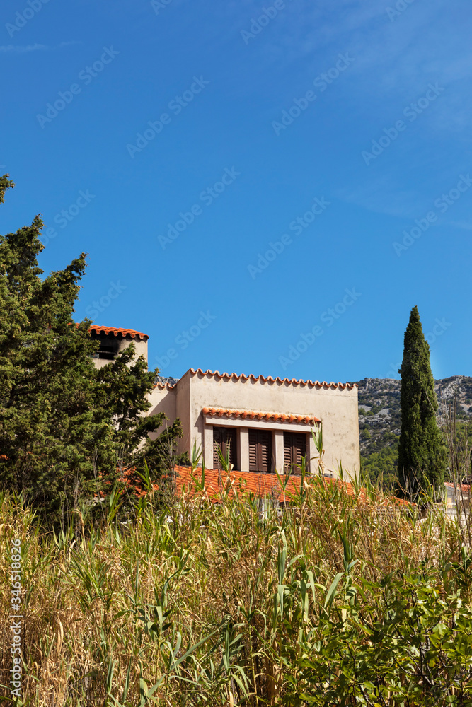A Mediterranean house with light colored facades and a orange roof at bol, Brac island, Dalmatia, Croatia on a sunny day in summer with greenery and a blue sky. Serene idyllic scenery