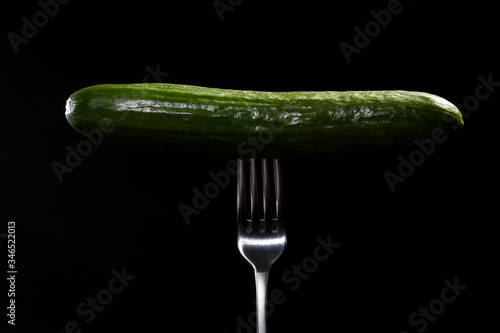 close up of fresh green cucumber on metal fork isolated on black background. Domestic cultivation. Fresh vegetables. Vegetarian dinner. © Andriy Medvediuk