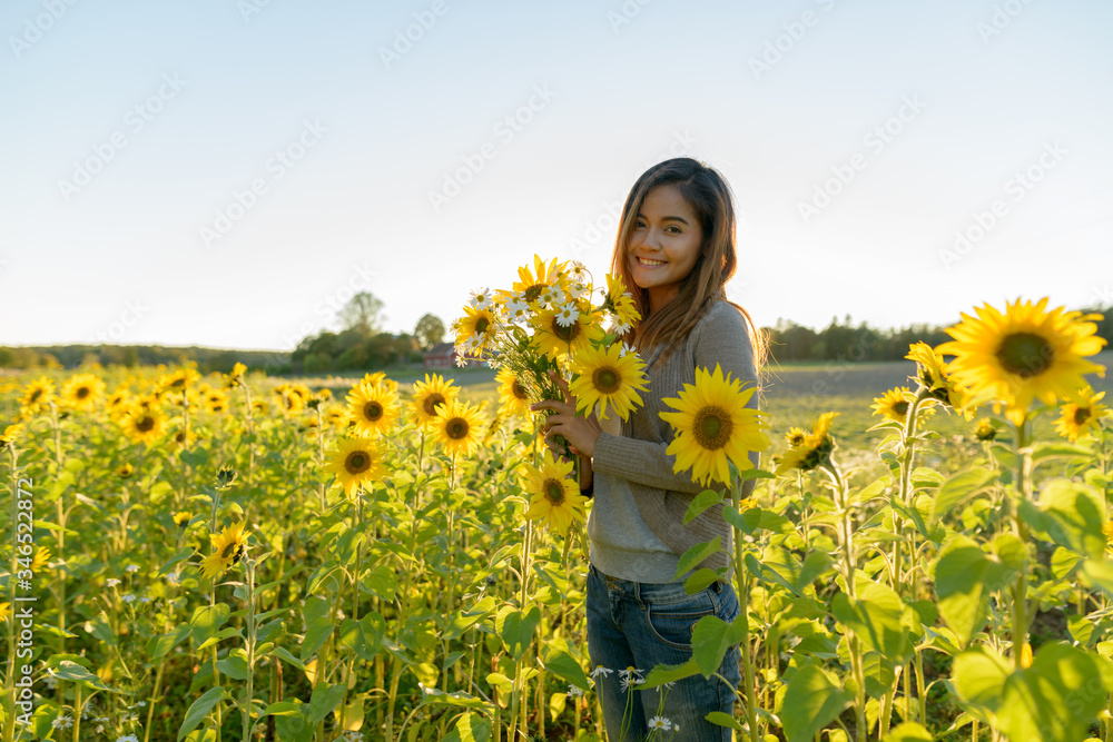 Fototapeta premium Happy young beautiful Asian woman holding flowers in the sunflower garden farm