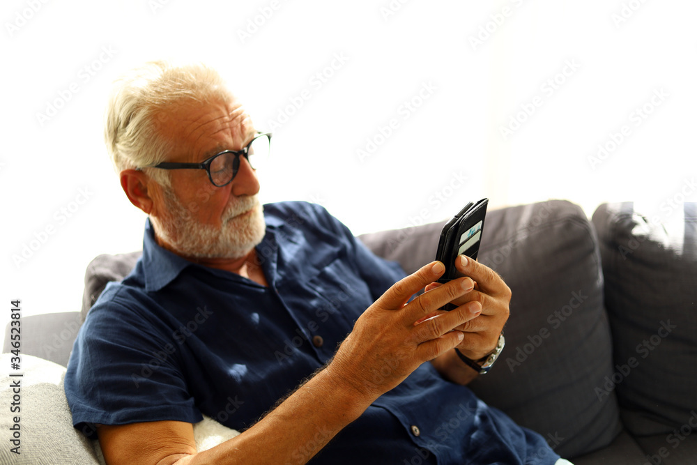 Fototapeta premium Elderly senior man sitting alone and playing mobile phone at home.