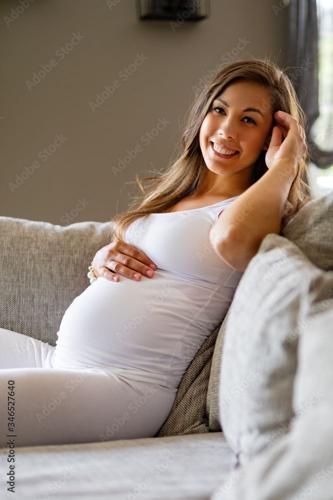 Happy beautiful pregnant woman sitting in sofa touching her belly Happy beautiful pregnant woman sitting in sofa touching her belly
