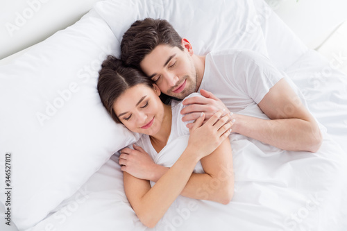 High angle above view photo charming cute lady husband guy couple lying comfortable sheets bed white blanket hugging joyful hold touch hands eyes closed wear pajama room indoors © deagreez