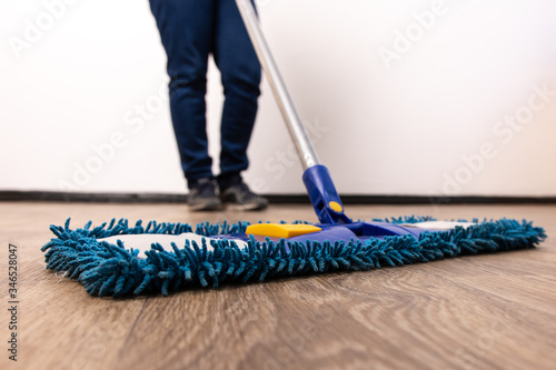 mop on the floor close-up. female legs in jeans on the background. general cleaning of the apartment. cleaning company at work.