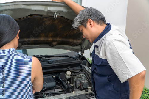 woman who owns the car standing and looking for auto mechanic Check the engine to find the cause.