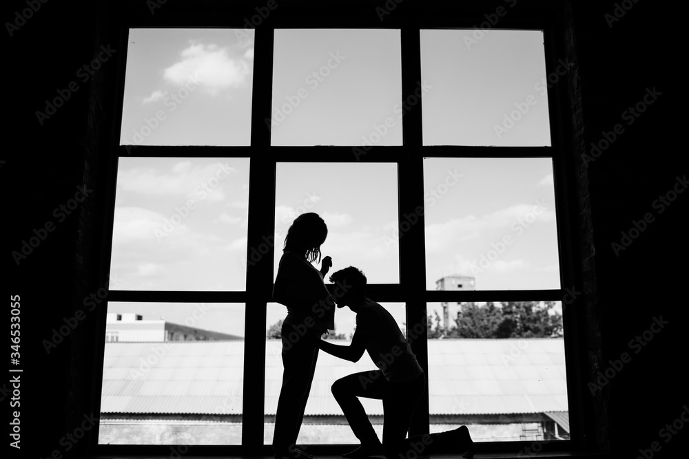 Silhouette of a couple in love. A man kneels and kisses a pregnant woman.