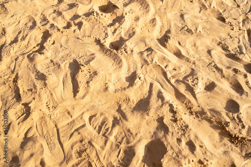 sand is trampled by a large number of different footprints from shoes. Traces are arranged randomly.