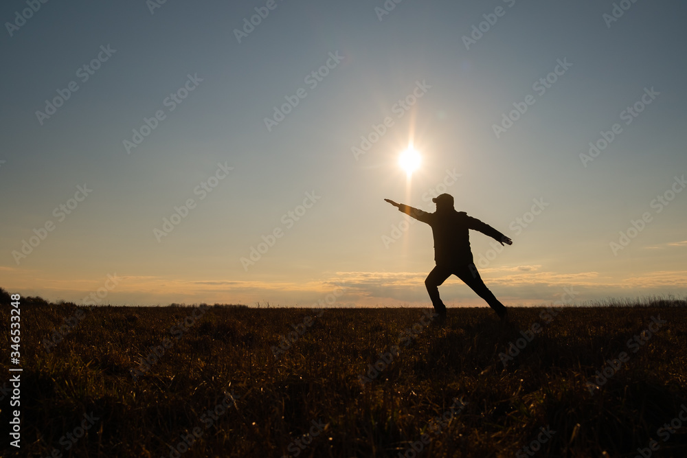 The contour of a man against the sky. The man spread his arms to the sides. One hand indicates upward direction. The concept of the joy of life and inner freedom of the world